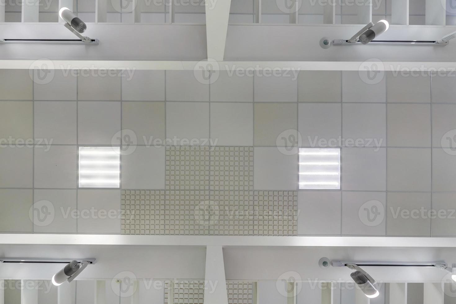 cassette suspended ceiling with square halogen spots lamps and drywall construction in empty room in apartment or house. Stretch ceiling white and complex shape. Looking up view photo