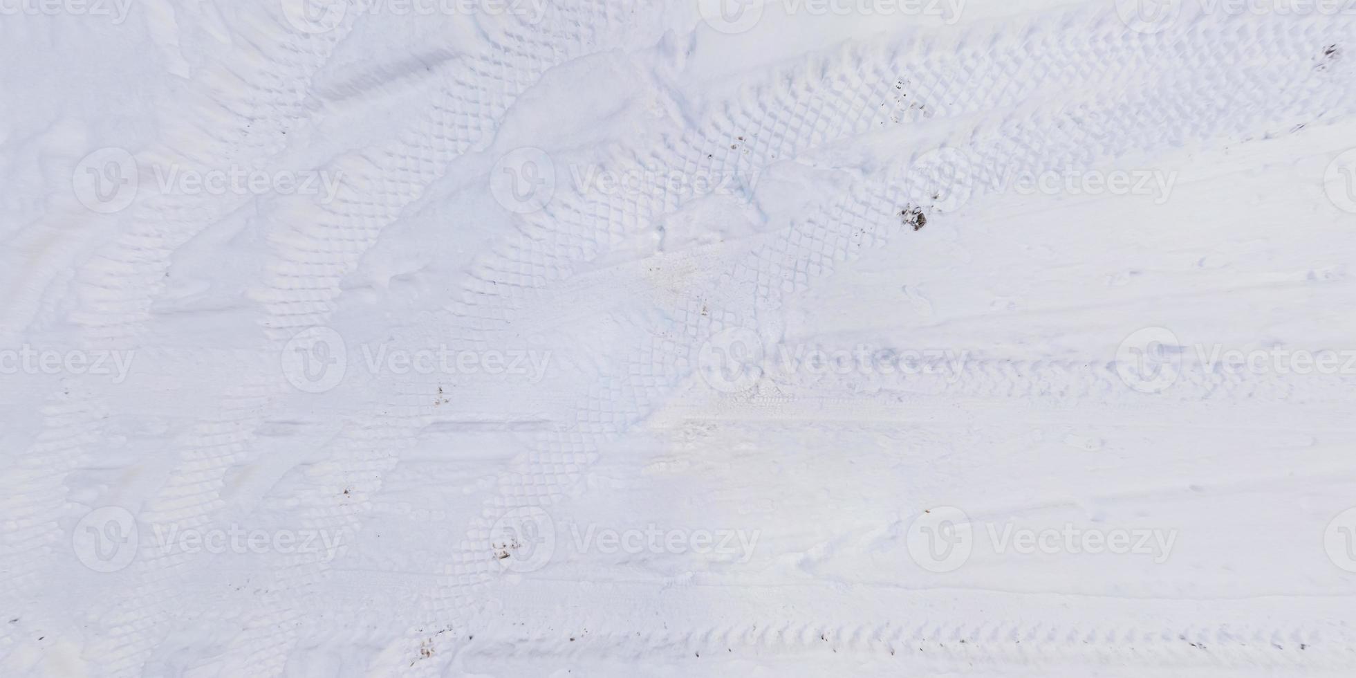 panorama view from above on texture of snow covered road with car tire tracks and footprints photo