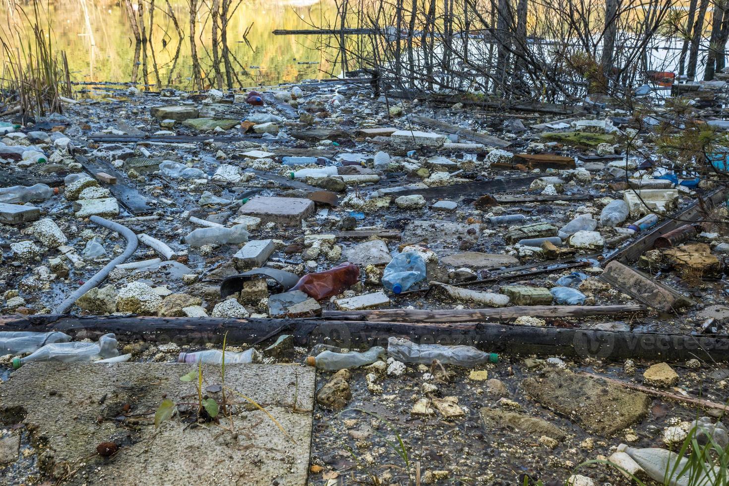 montones de residuos de construcción, residuos domésticos, espuma y botellas de plástico en la orilla de un lago forestal, problemas de contaminación ambiental foto