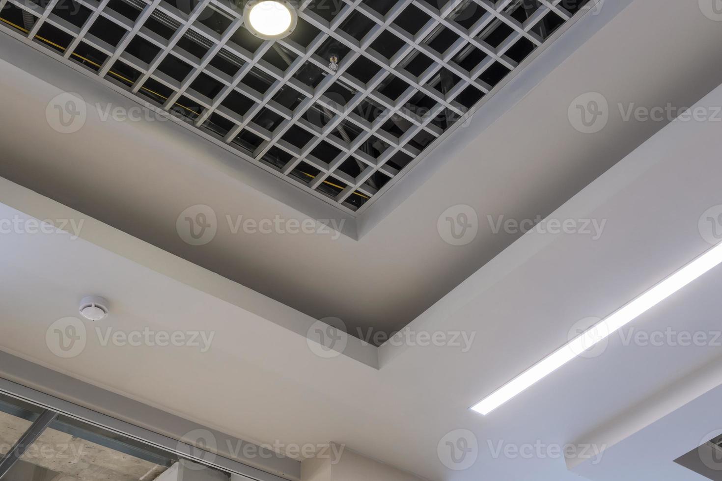 suspended and grid ceiling with halogen spots lamps and drywall construction in empty room in store or house. Stretch ceiling white and complex shape. photo