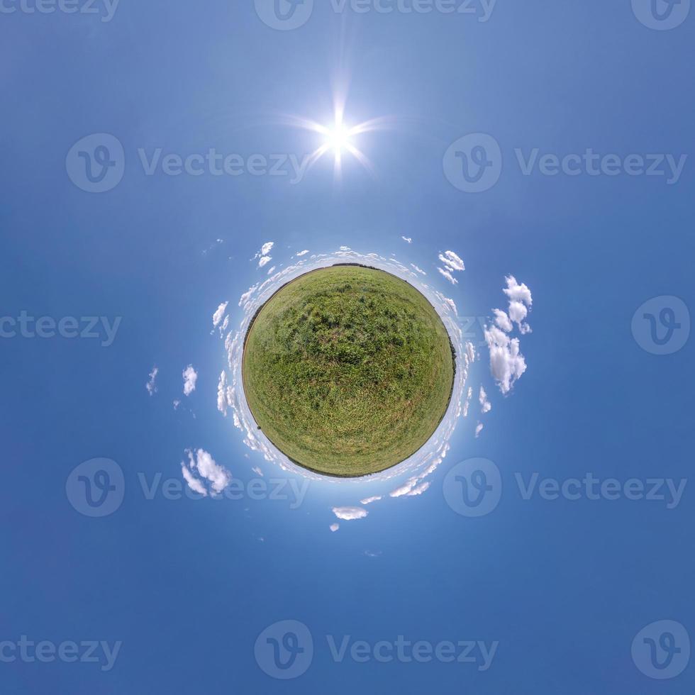 green tiny planet in blue sky with sun and beautiful clouds. Transformation of spherical panorama 360 degrees. Spherical abstract aerial view. Curvature of space. photo