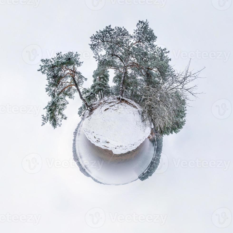 Winter tiny planet in snow covered pinery forest near lake with transformation of spherical panorama 360 degrees in abstract aerial view in forest. Curvature of space photo