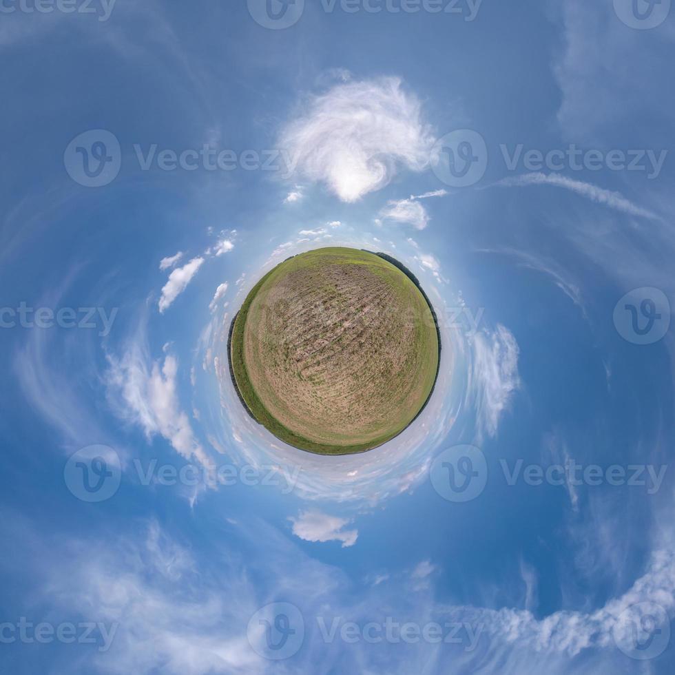 green tiny planet in blue sky with beautiful clouds. Transformation of spherical panorama 360 degrees. Spherical abstract aerial view. Curvature of space. photo
