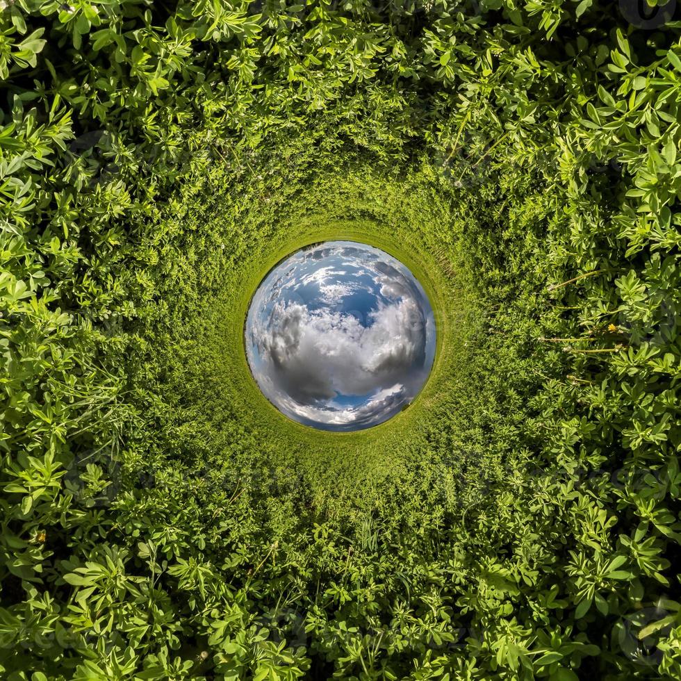 Inversion of blue tiny planet transformation of spherical panorama 360 degrees. Spherical abstract aerial view on green grass field with awesome beautiful clouds. Curvature of space. photo