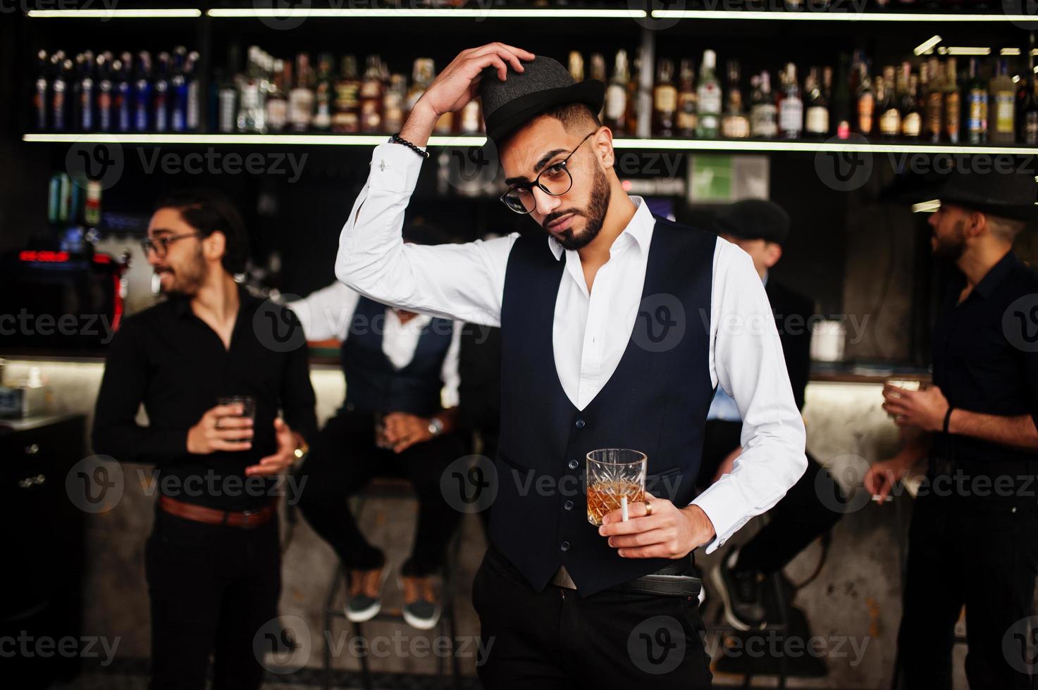 Stylish arab man against group of handsome retro well-dressed guys gangsters spend time at club, drinking on bar counter. Multiethnic male bachelor mafia party in restaurant. photo