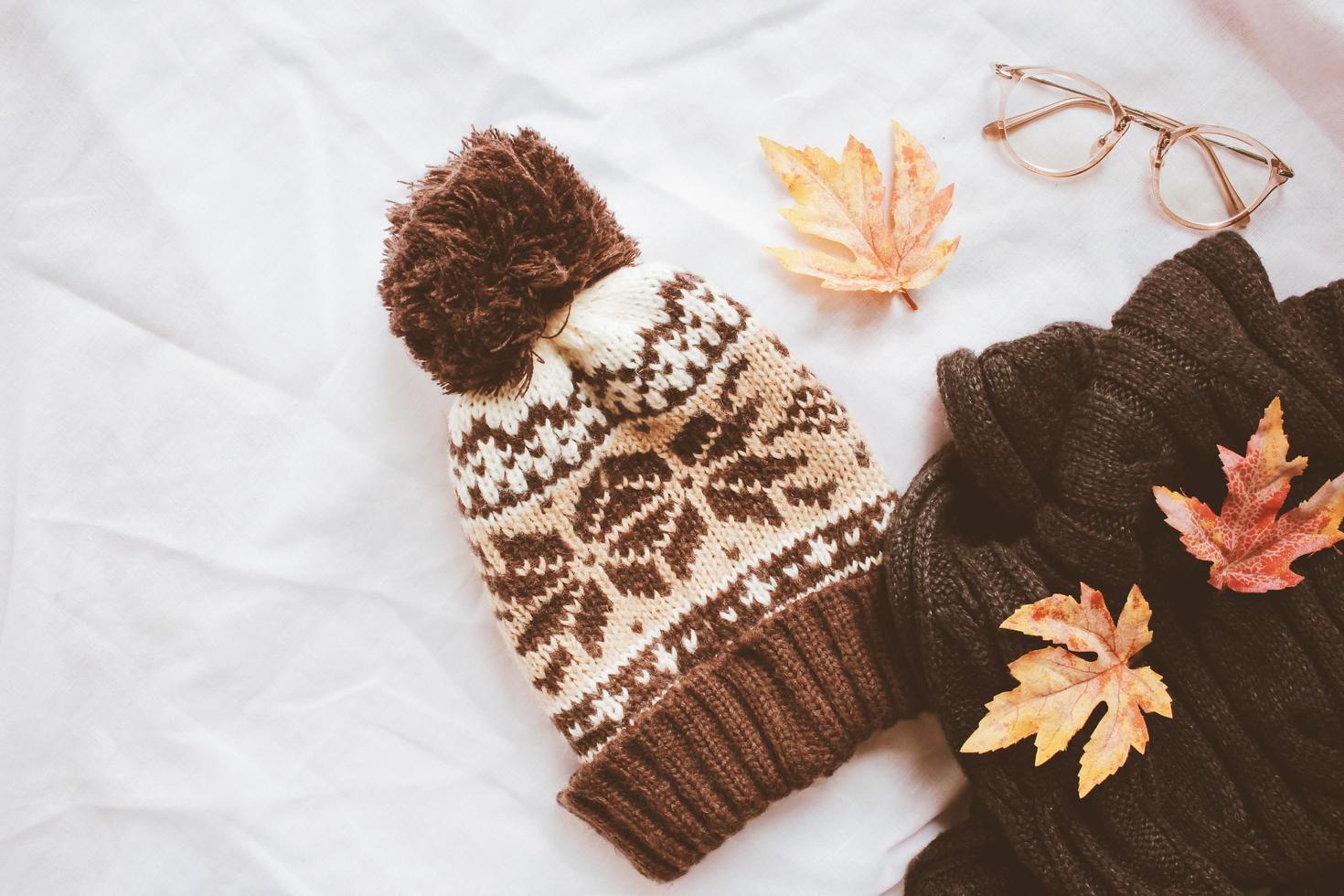 endecha plana de estilo de moda de otoño, bufanda, gorro de punto y anteojos con hojas de arce sobre fondo de sábana blanca foto