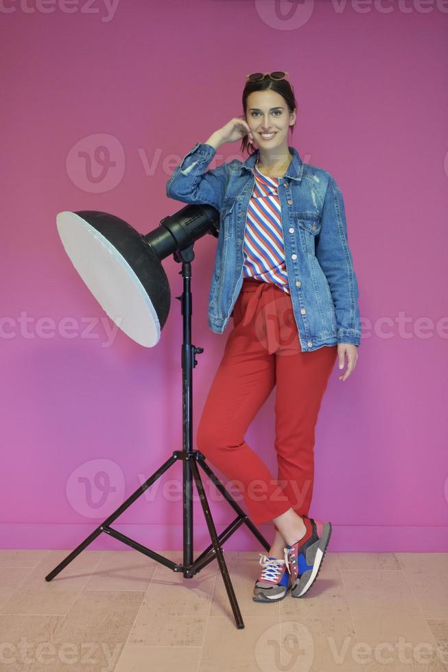 Young woman leaning against studio flashlight over a pink background photo