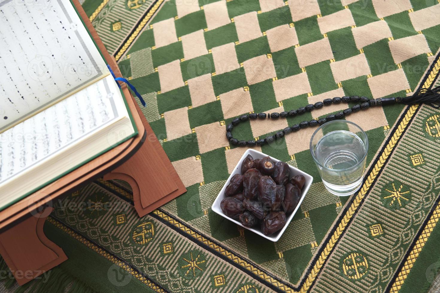 Iftar time dried dates holy Quran  glass of water and tasbih on praying  rug or sejadah photo