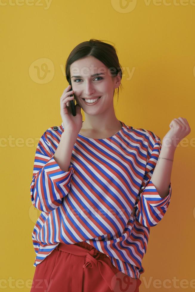 Portrait of young girl talking on the phone while standing in front of yellow background photo