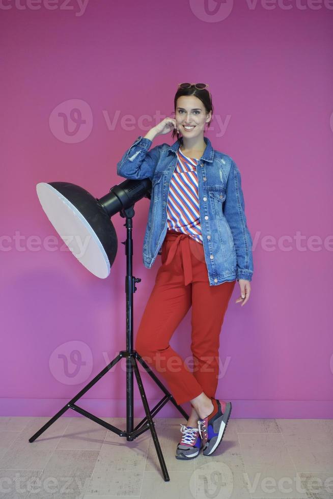 Young woman leaning against studio flashlight over a pink background photo
