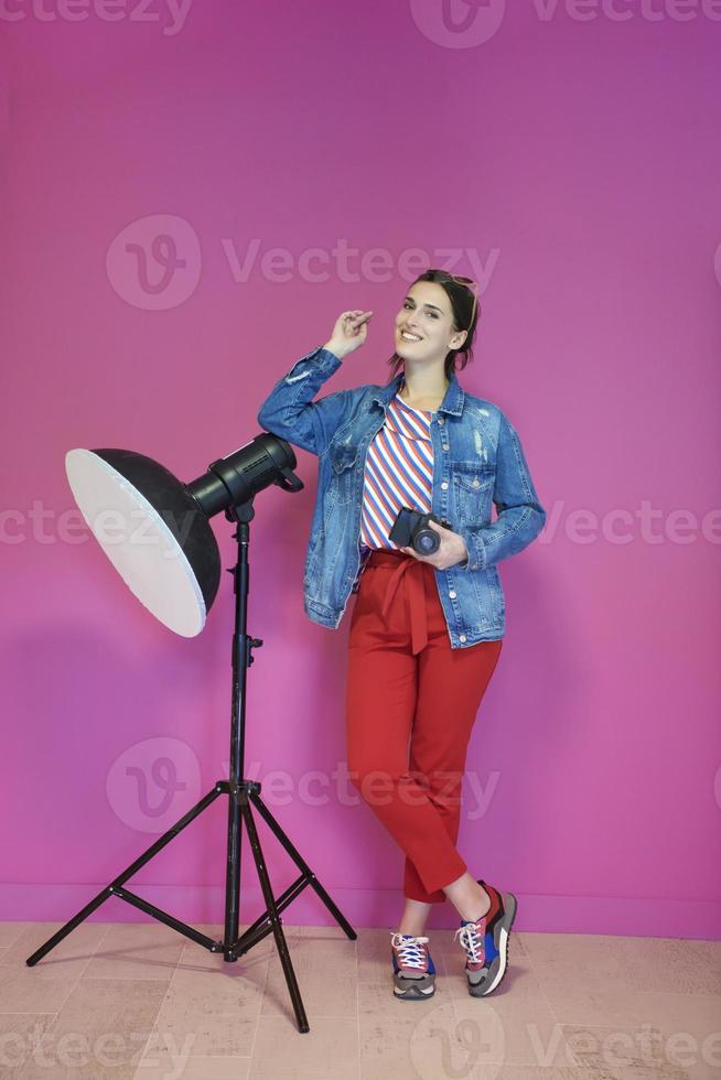 mujer joven apoyada contra la linterna del estudio y sosteniendo la cámara sobre un fondo rosa foto