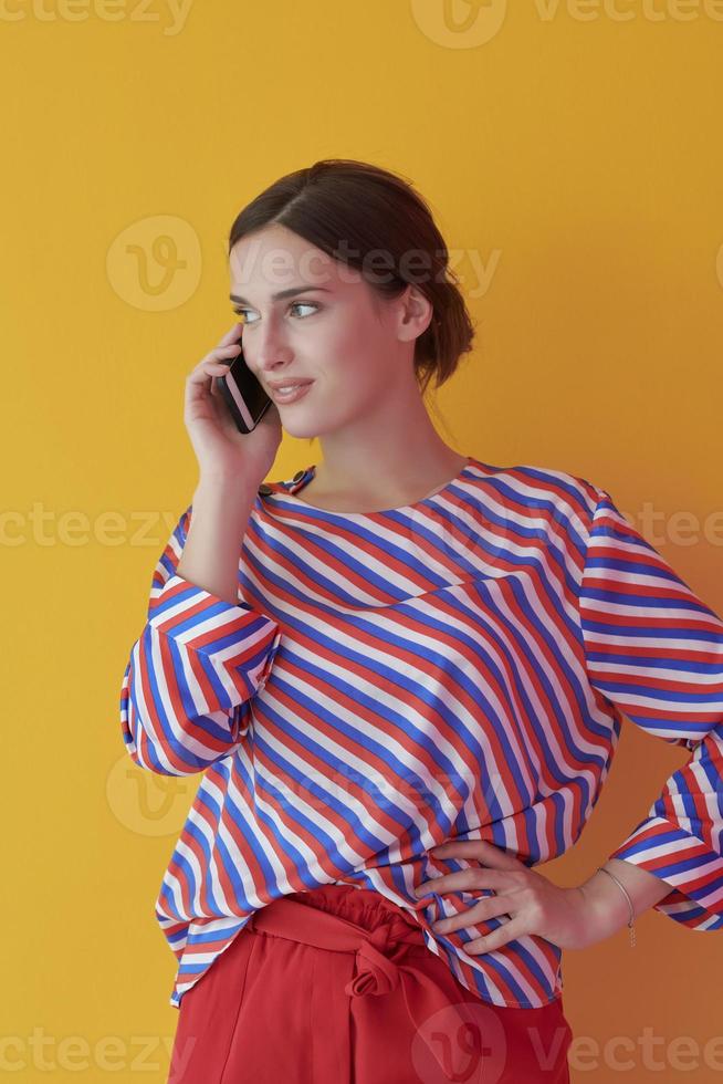 Portrait of young girl talking on the phone while standing in front of yellow background photo