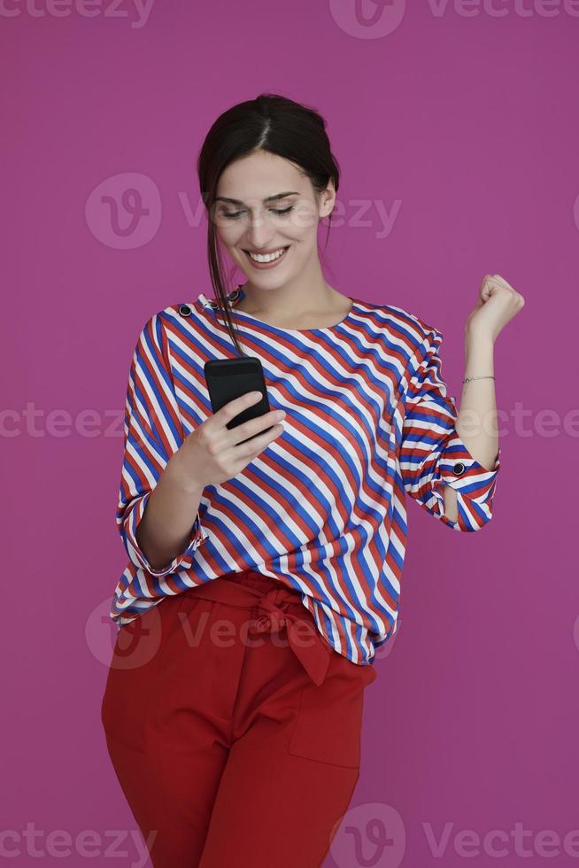 Portrait of young girl with happy face while using smartphone isolated on pink background photo