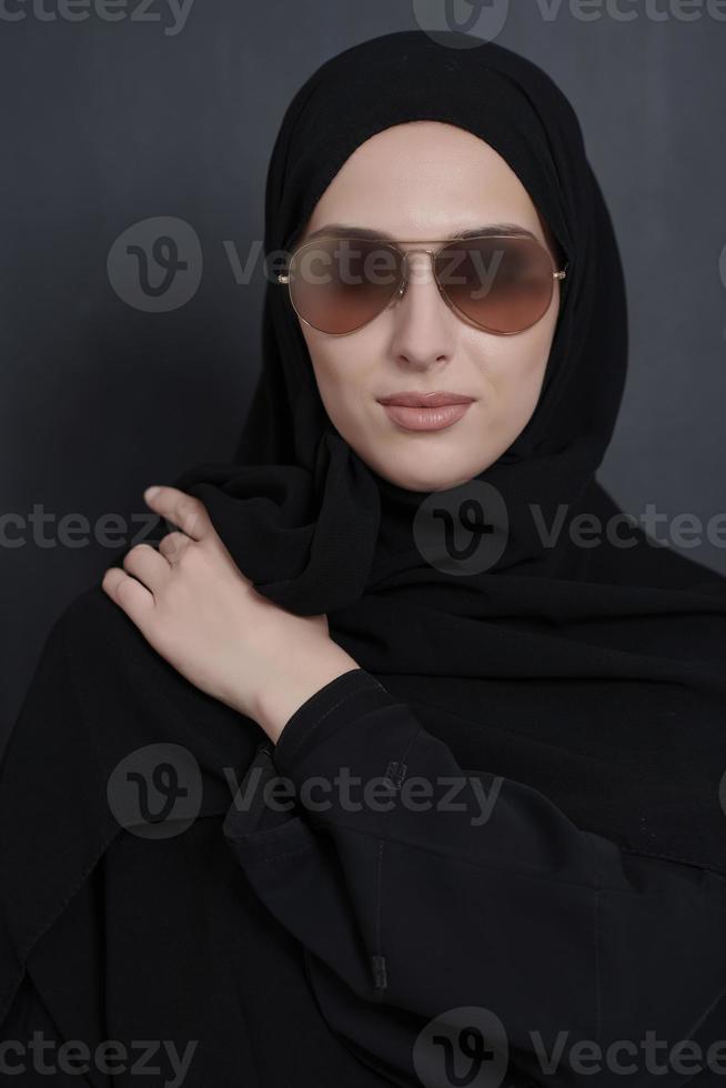 joven mujer de negocios musulmana con ropa tradicional o abaya y gafas de sol posando frente a una pizarra negra foto