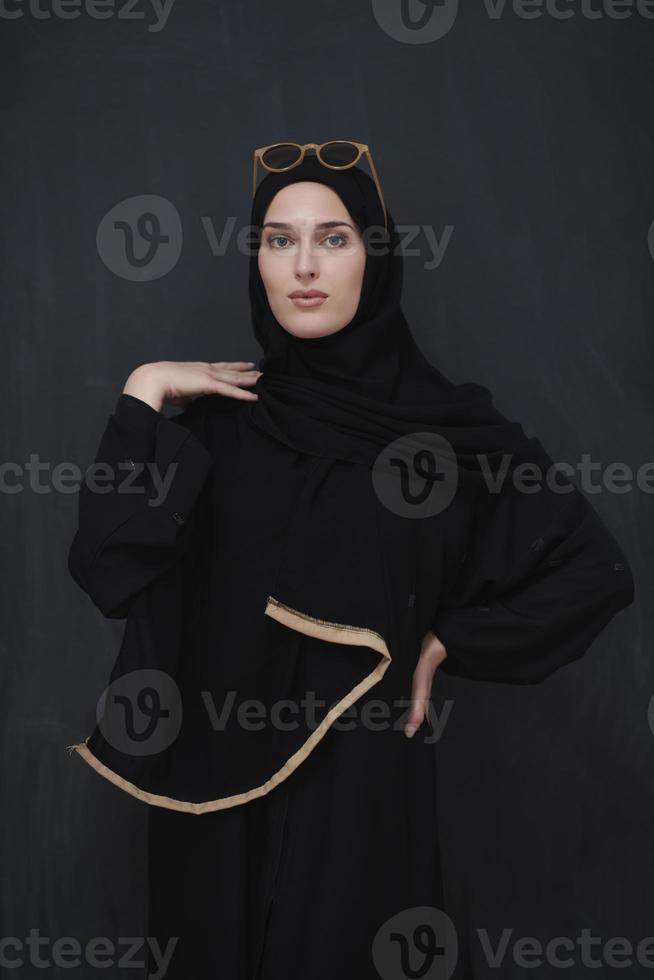 Young muslim in traditional clothes or abaya and sunglasses posing in front of black chalkboard photo