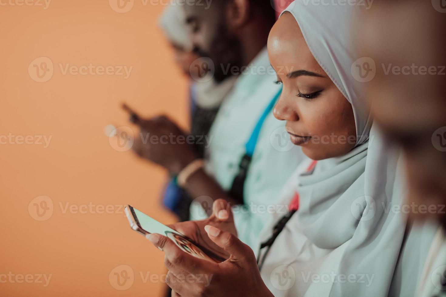 A group of African Muslim students use smartphones while standing in front of a yellow background photo