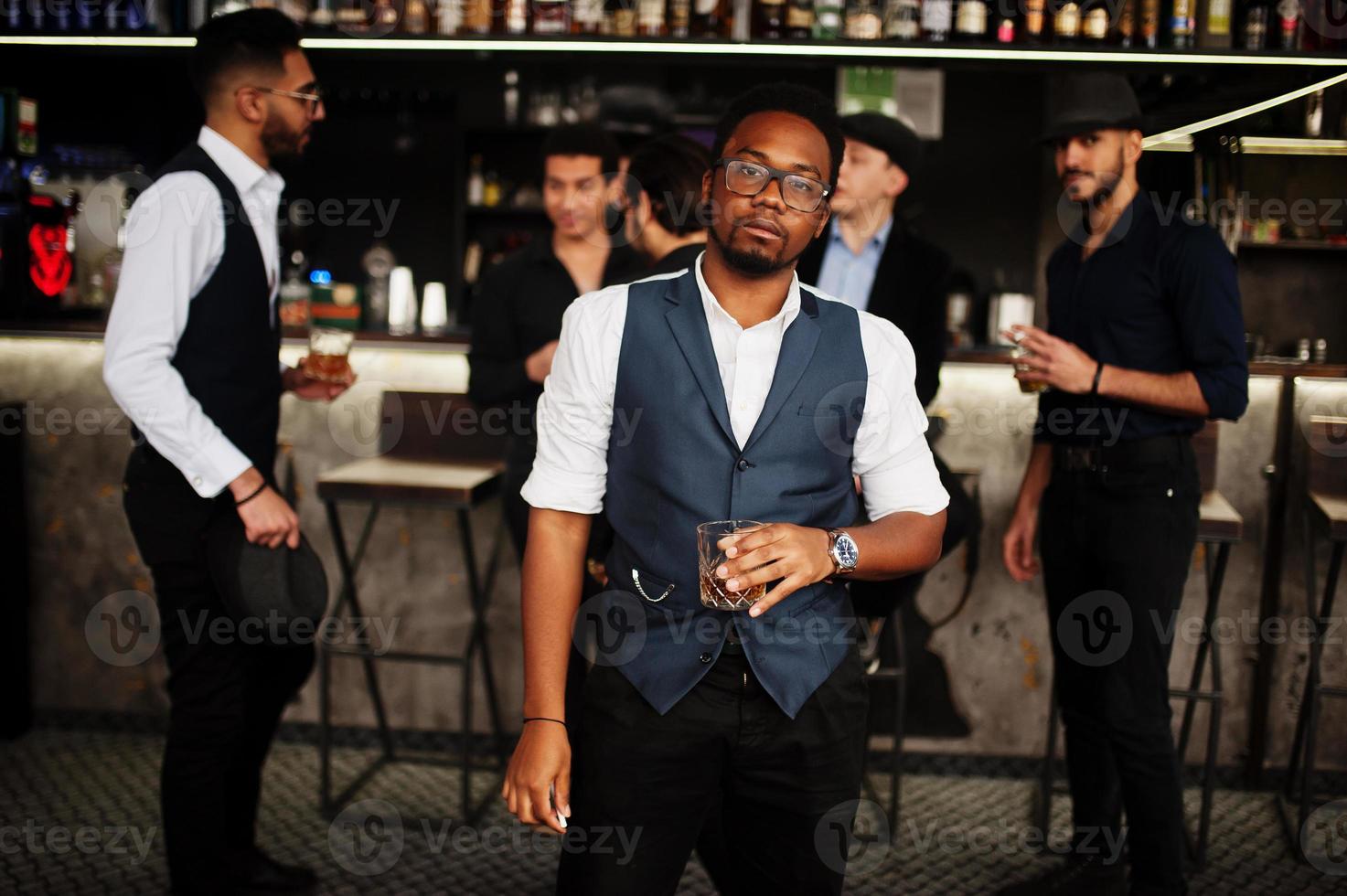 Stylish african american man against group of handsome retro well-dressed guys gangsters spend time at club, drinking on bar counter. Multiethnic male bachelor mafia party in restaurant. photo