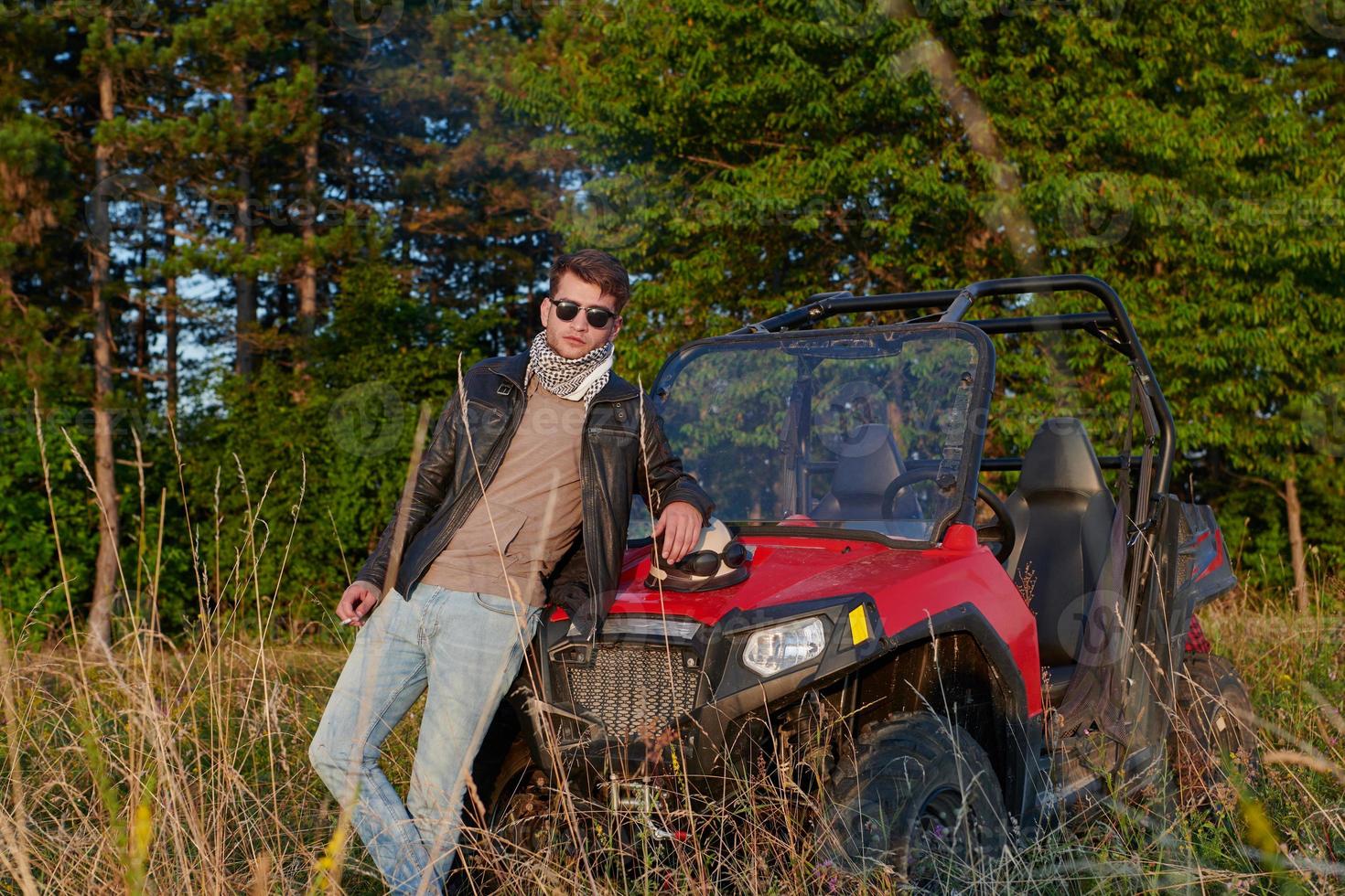 hombre disfrutando de un hermoso día soleado fumando un cigarrillo mientras toma un descanso de conducir un coche de buggy todoterreno foto