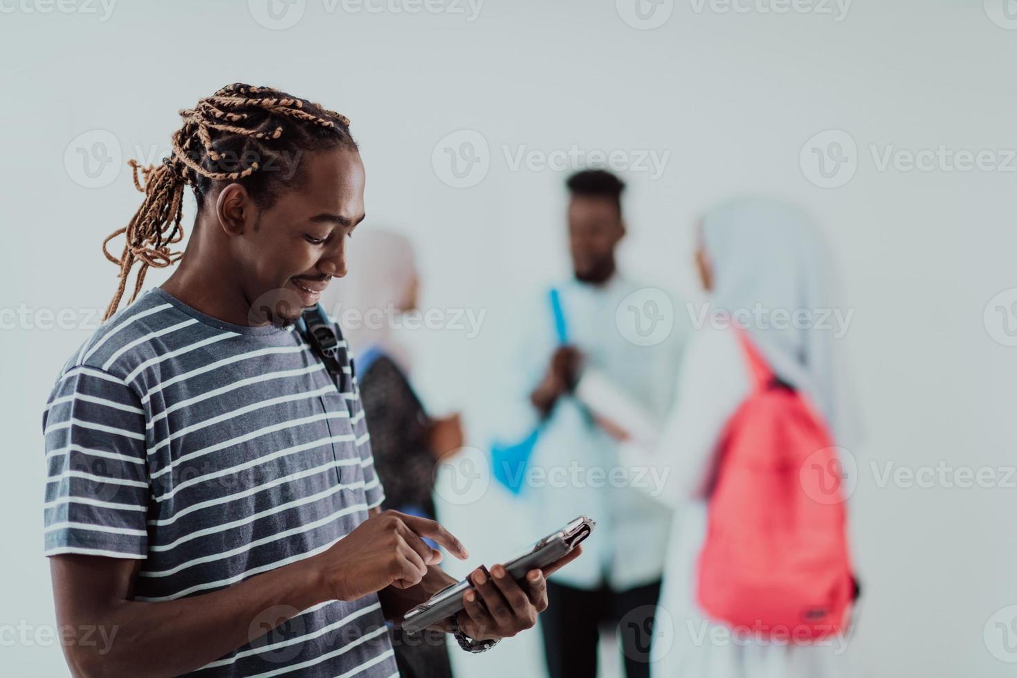 University lifestyle student holding a tablet computer and smiling while standing against university with his friends have a team meeting in the background. High-quality photo