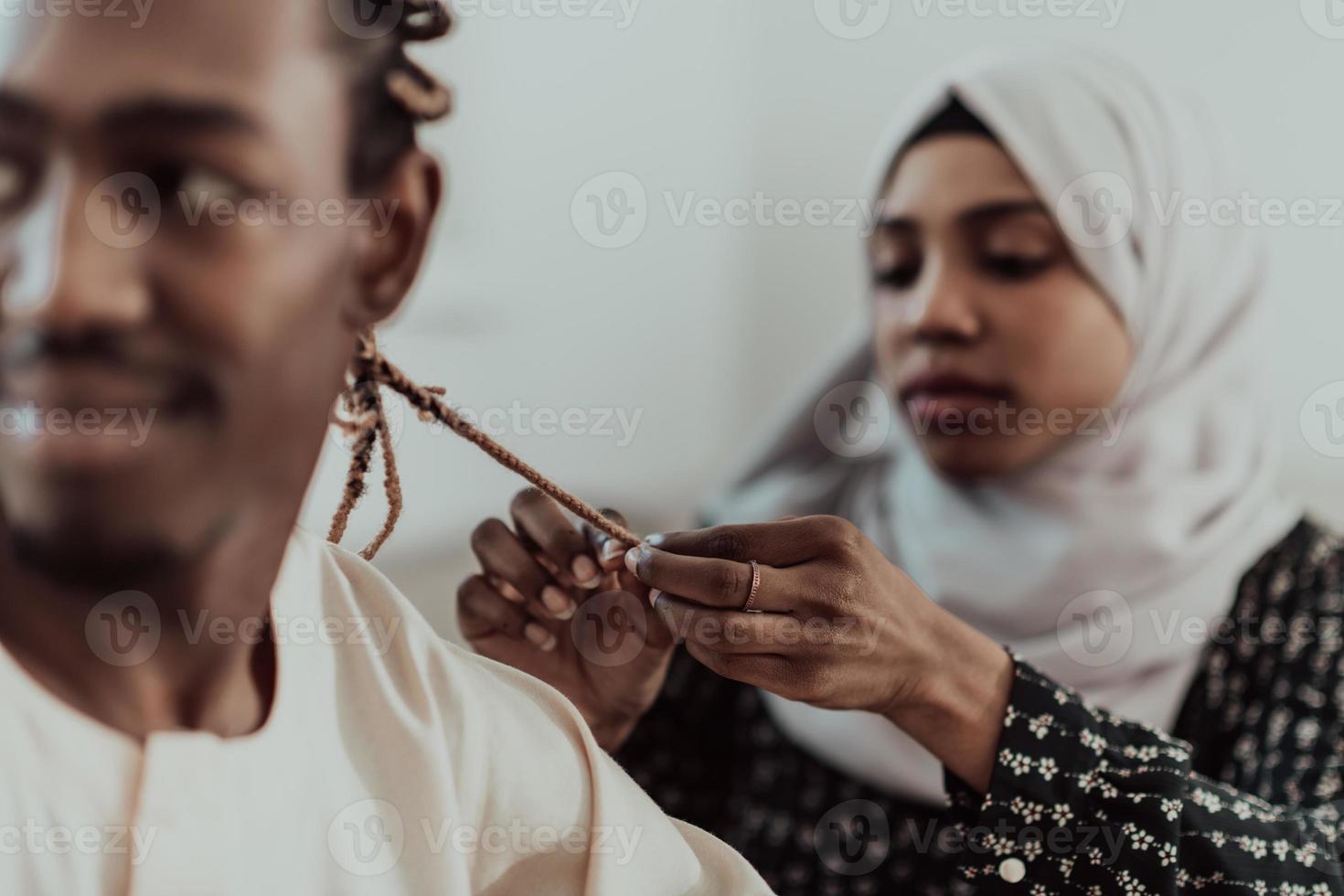 A young Muslim couple has a romantic time at home while the woman makes the hairstyle for her husband female wearing traditional Sudan Islamic hijab clothes. photo