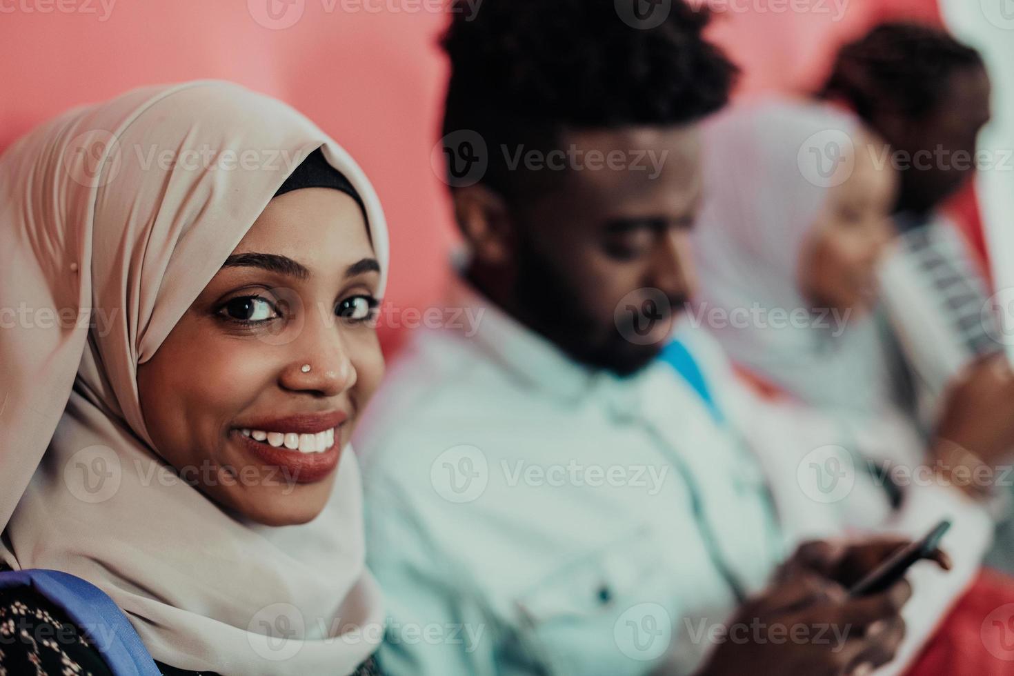 A group of African Muslim students use smartphones while standing in front of a pink background photo