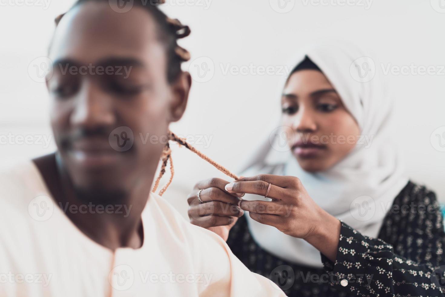 A young Muslim couple has a romantic time at home while the woman makes the hairstyle for her husband female wearing traditional Sudan Islamic hijab clothes. photo