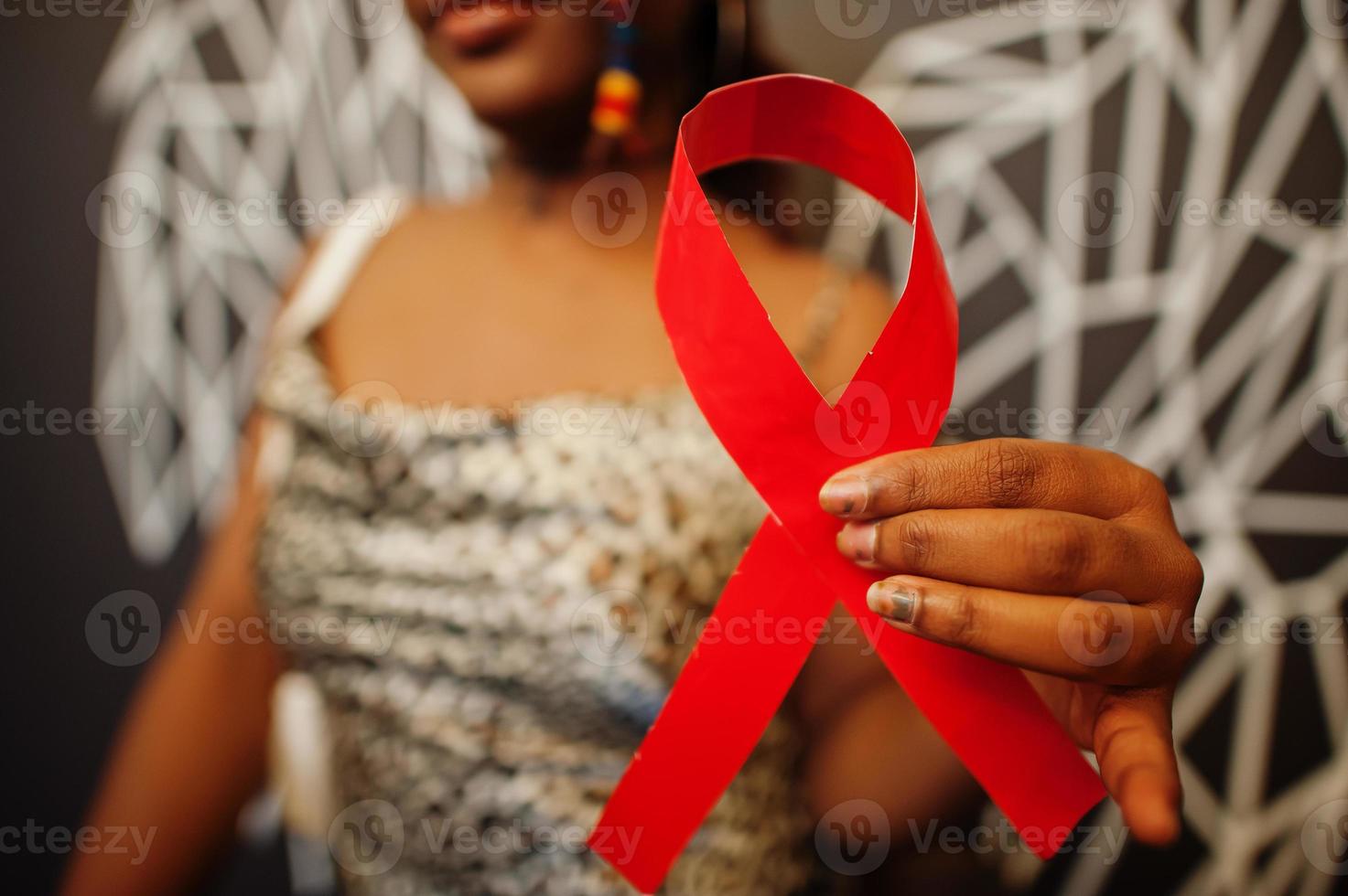 AIDS awareness. Stylish african american woman hold red ribbon against wall with wings. photo