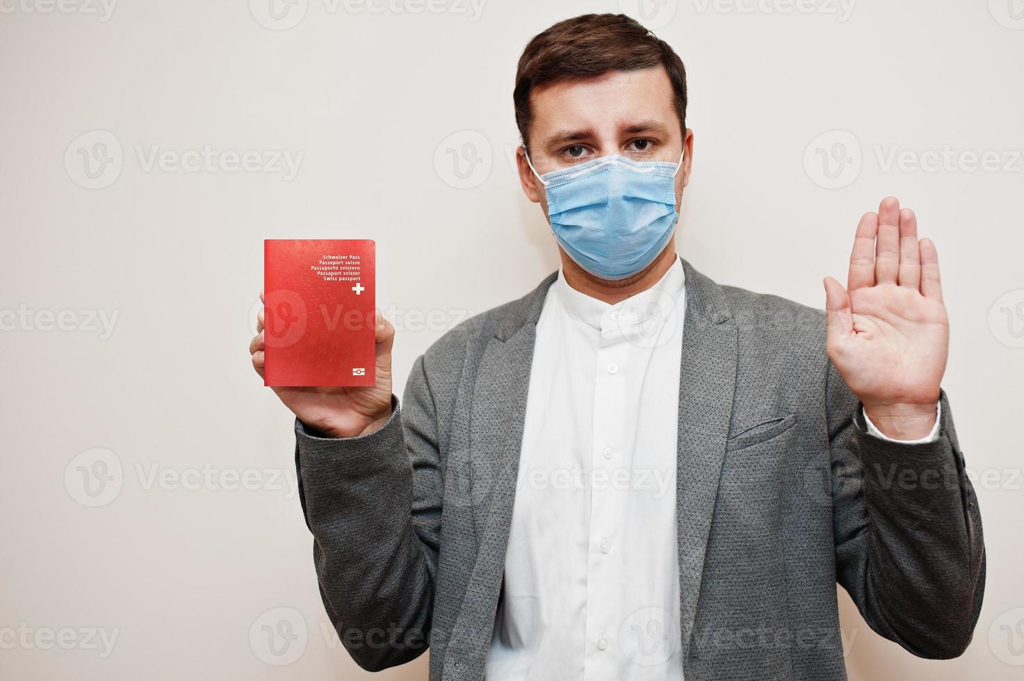 European man in formal wear and face mask, show Switzerland passport with stop sign hand. Coronavirus lockdown in Europe country concept. photo