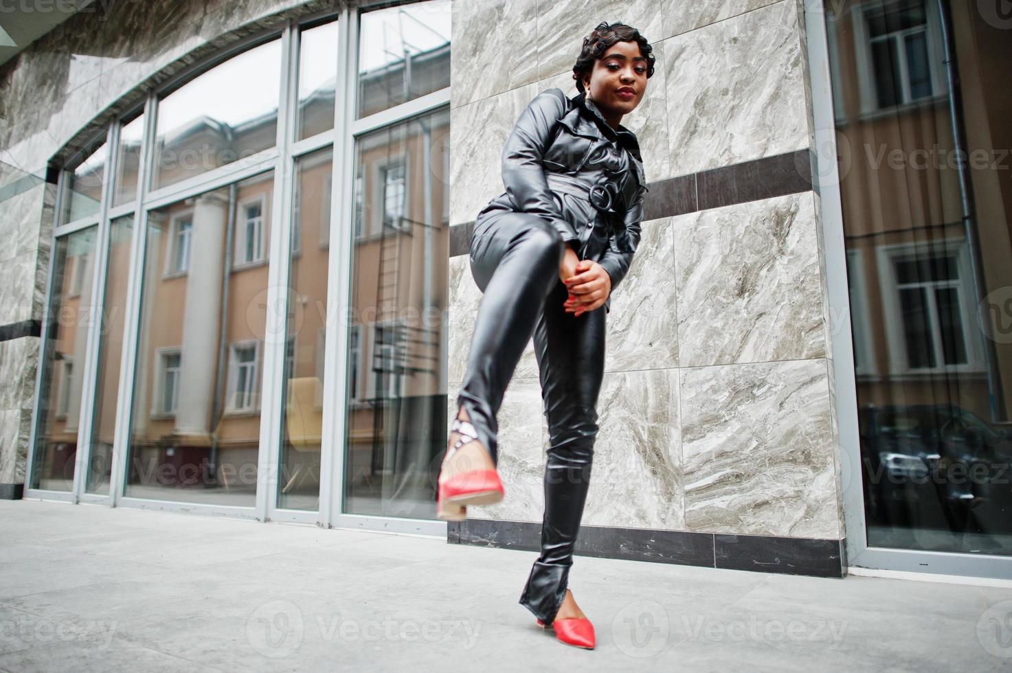 Fashionable beautiful african american woman posing in black leather jacket and pants at street. photo