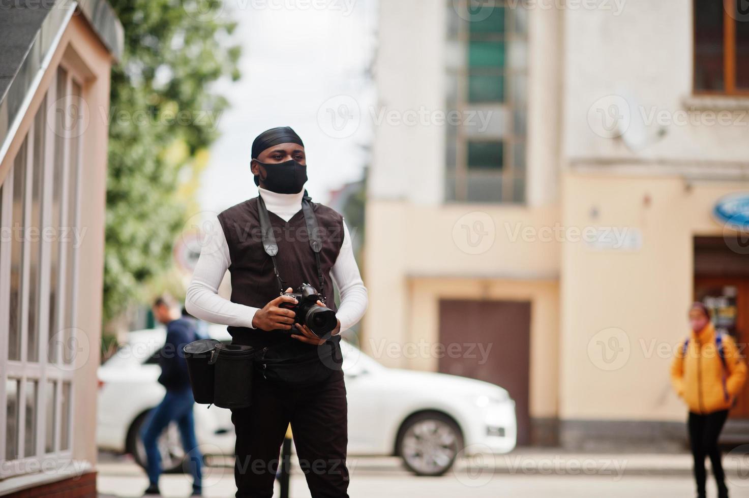 Young professional african american videographer holding professional camera with pro equipment. Afro cameraman wearing black duraq and face protect mask, making a videos. photo