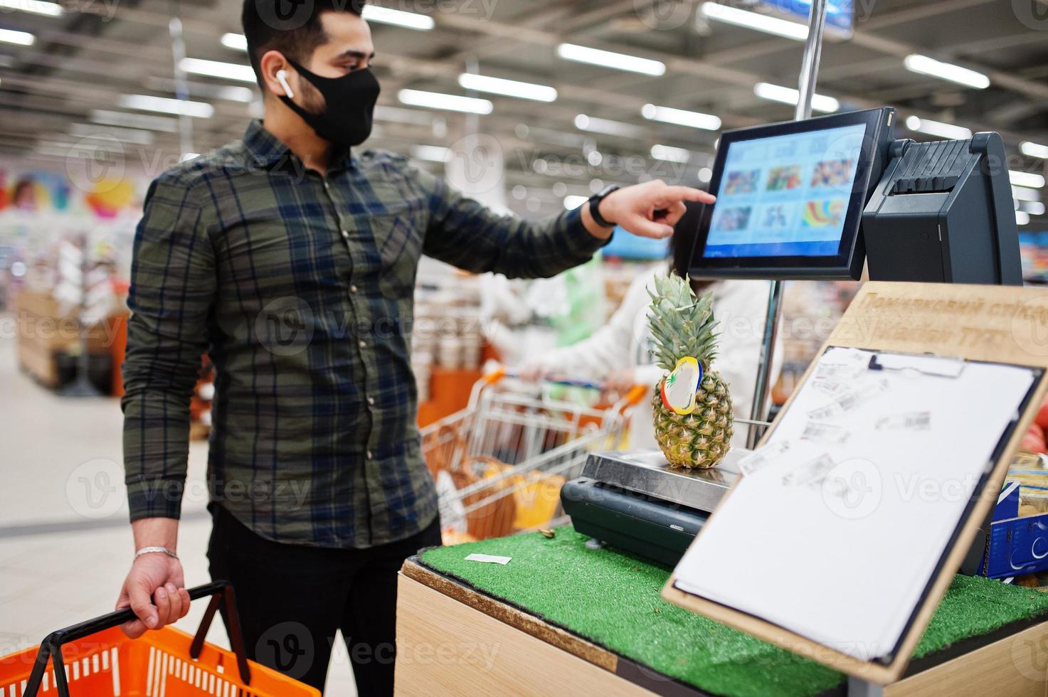 Asian man wear in protective face mask shopping in supermarket during pandemic.  Weigh pineaple. photo