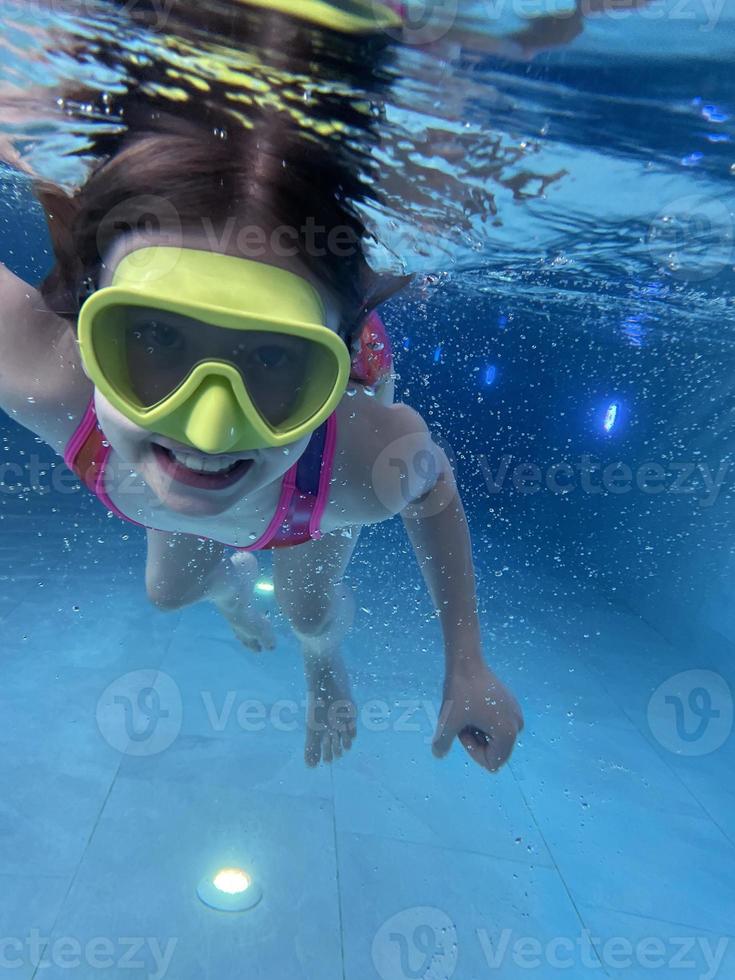 Smiling child in goggles swim, dive in the pool with fun - jump deep down underwater. Healthy lifestyle, people water sport activity on summers. photo