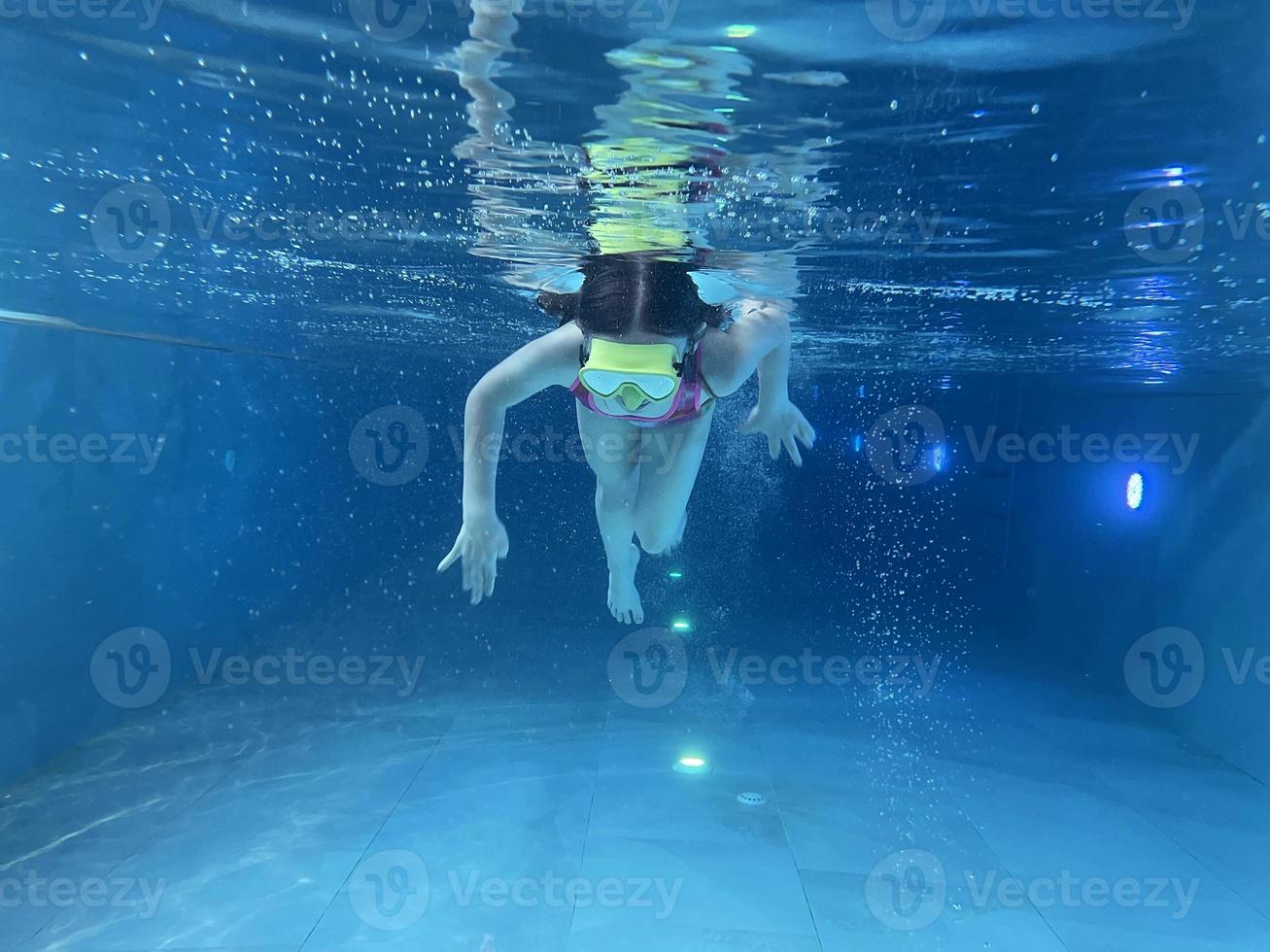 un niño sonriente con gafas nada, se sumerge en la piscina con diversión, salta profundamente bajo el agua. estilo de vida saludable, actividad de deportes acuáticos en los veranos. foto