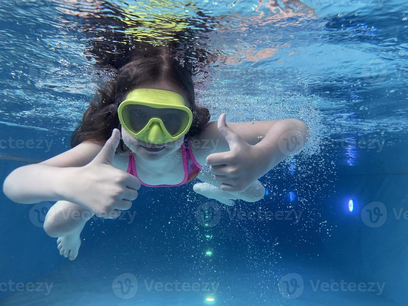 un niño sonriente con gafas nada, se sumerge en la piscina con diversión, salta profundamente bajo el agua. estilo de vida saludable, actividad de deportes acuáticos en los veranos. foto