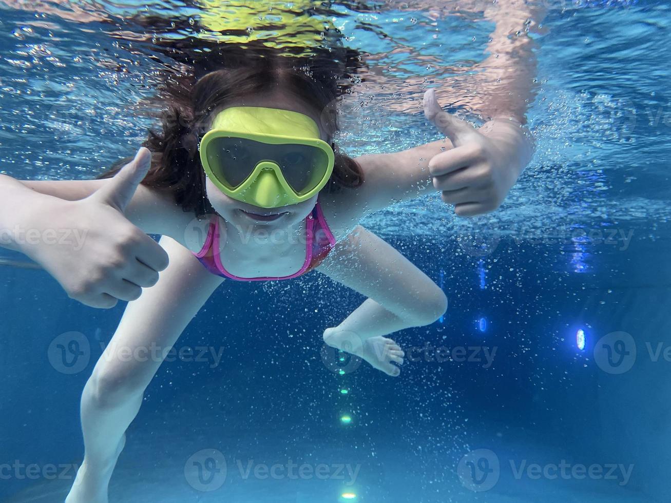 un niño sonriente con gafas nada, se sumerge en la piscina con diversión, salta profundamente bajo el agua. estilo de vida saludable, actividad de deportes acuáticos en los veranos. foto