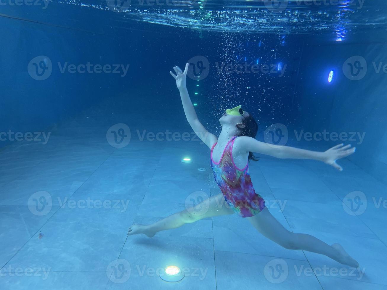 un niño sonriente con gafas nada, se sumerge en la piscina con diversión, salta profundamente bajo el agua. estilo de vida saludable, actividad de deportes acuáticos en los veranos. foto