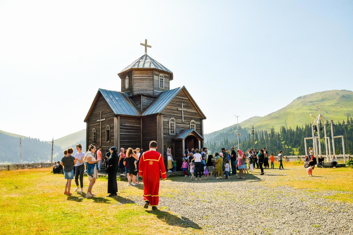 Bakhmaro, Georgia, 2022-priest in red coat walk by Bakhmaro church to Sunday mass with village people outside socialize photo