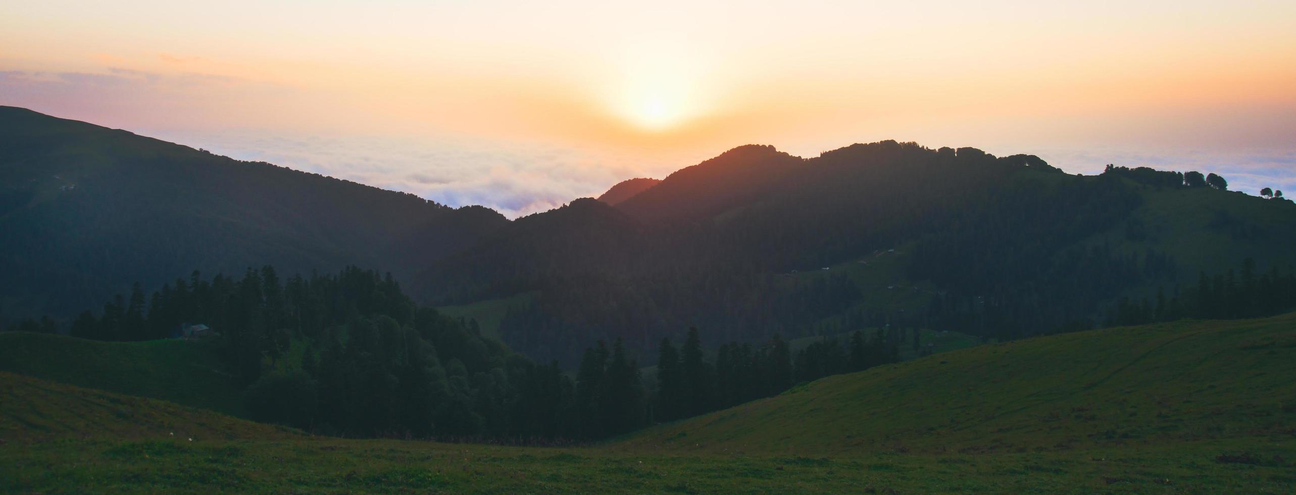 Wide aerial panoramic view of sun rising above horizon with clouds above forest. Weather and forecast background photo