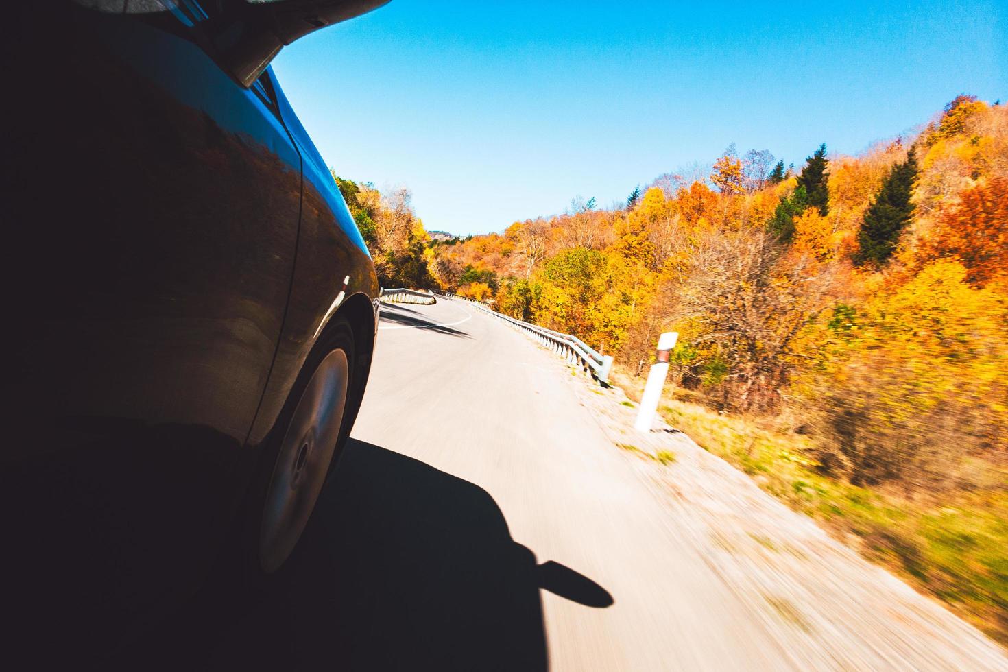 Fast motion car wheel spins fast on asphalt road with autumn nature trees and landscape on serpentine road. Travel in calm summer evening and road trip concept. Intentional blur filter affect photo