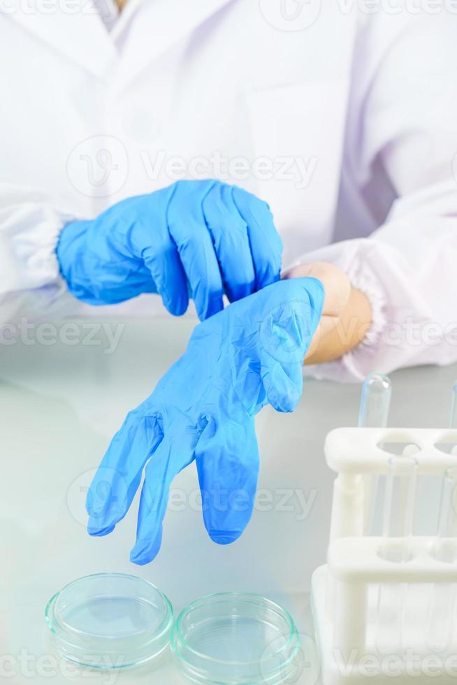 Manos científicas poniéndose guantes de látex azul de nitrilo en una bata de laboratorio usando guantes de nitrilo foto