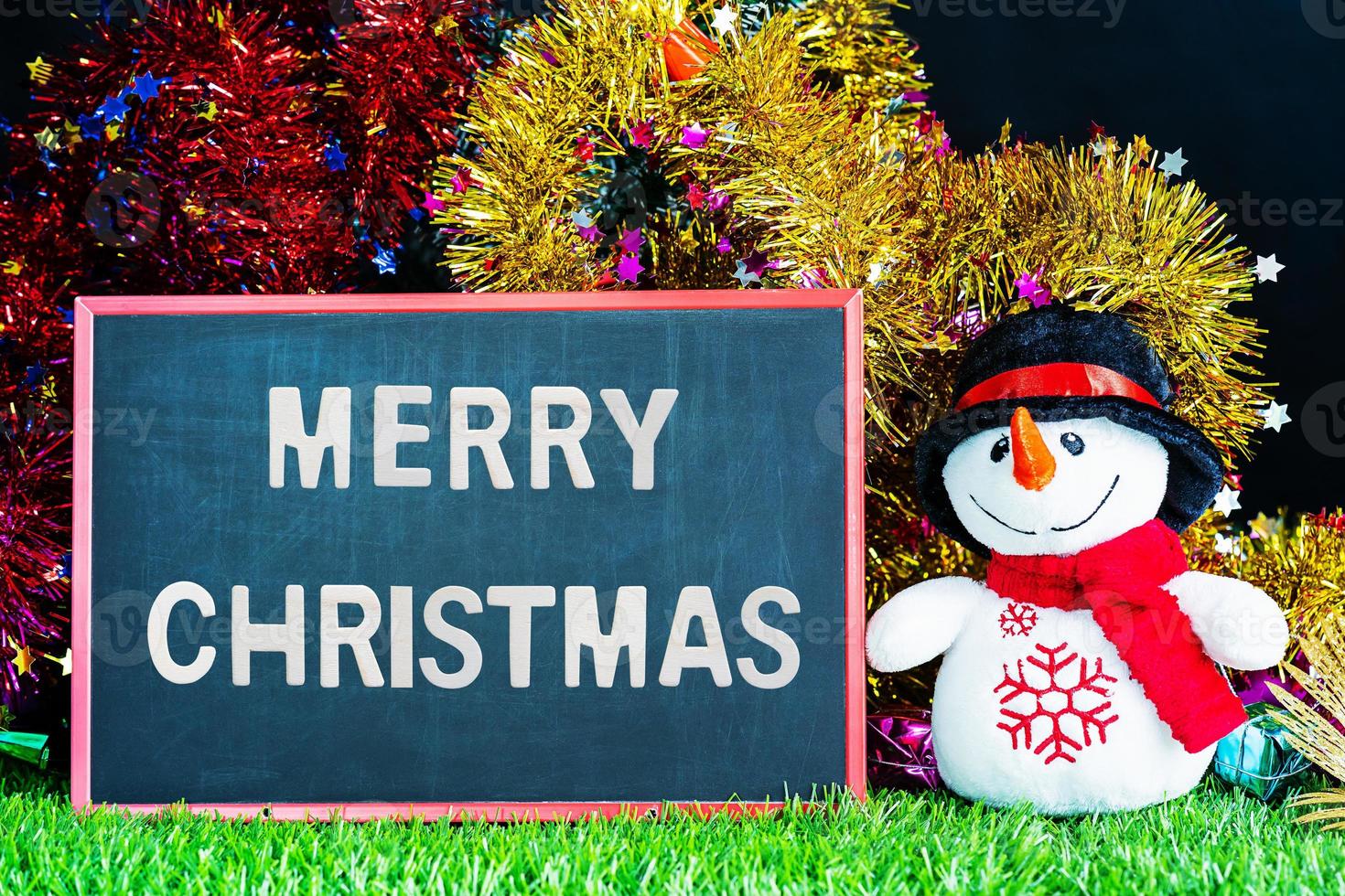Doll snowman on green grass with chalkboard photo