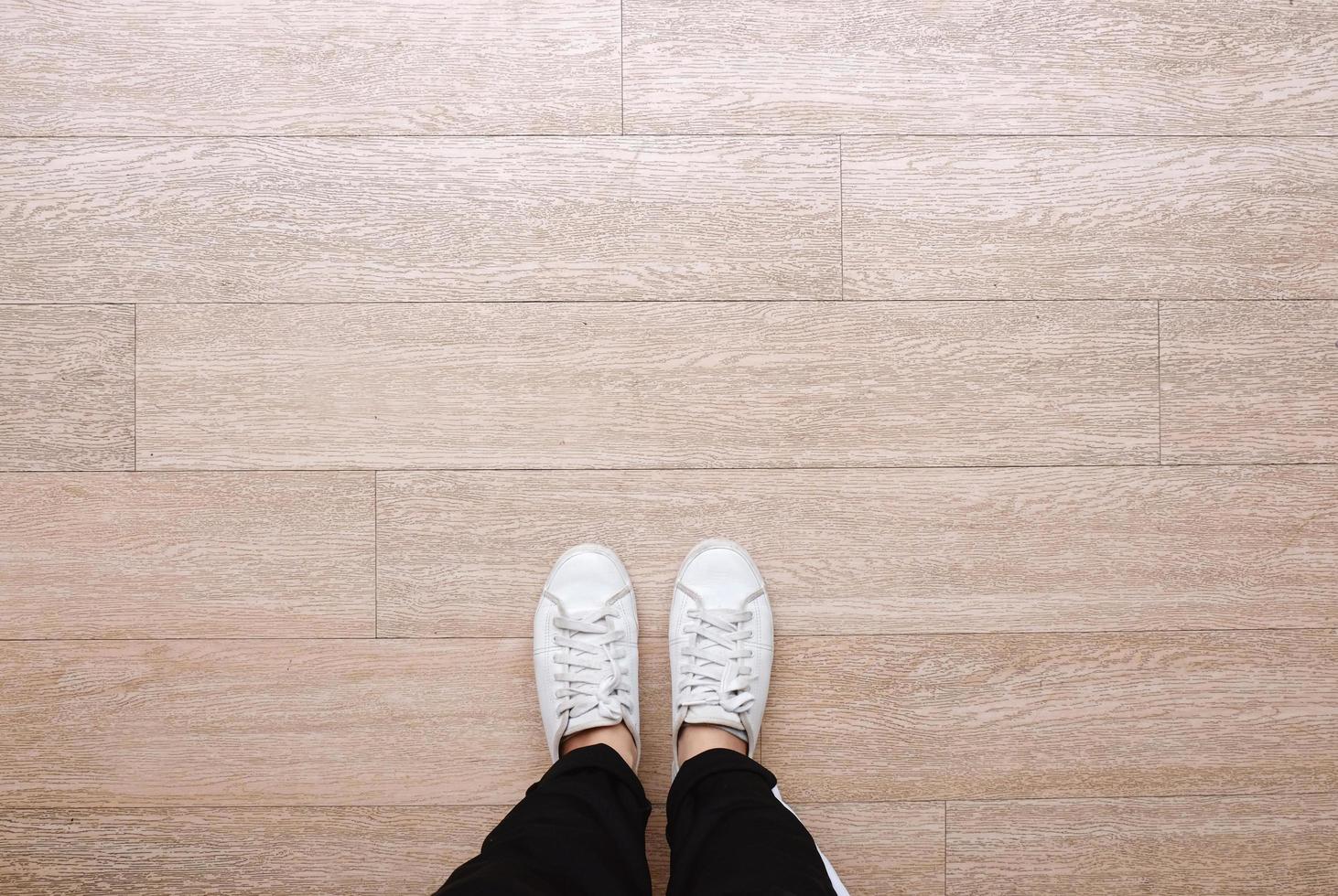 Selfie of feet in fashion sneakers on wooden floor background, top view with copy space photo