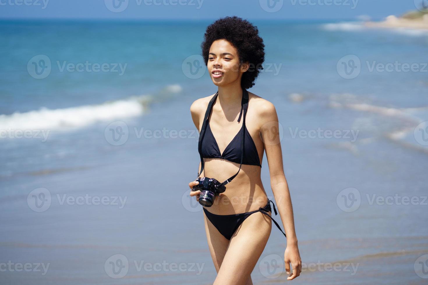 Black woman in swimsuit with photo camera at seaside
