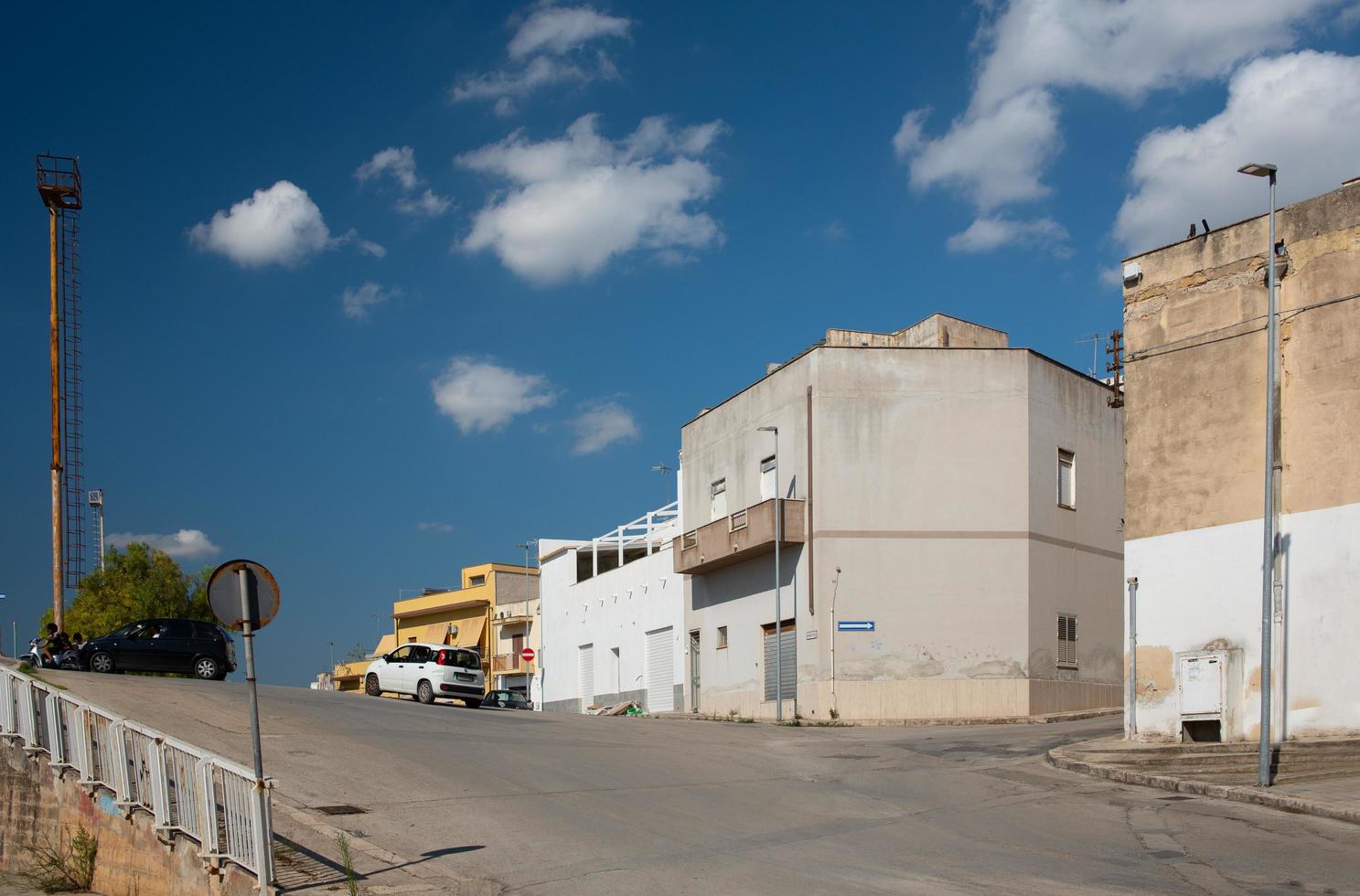 Typical street scene of a town in Sicily in summer around noon. Houses stand at the side of the road, a road rises and white clouds drift across the blue sky. photo