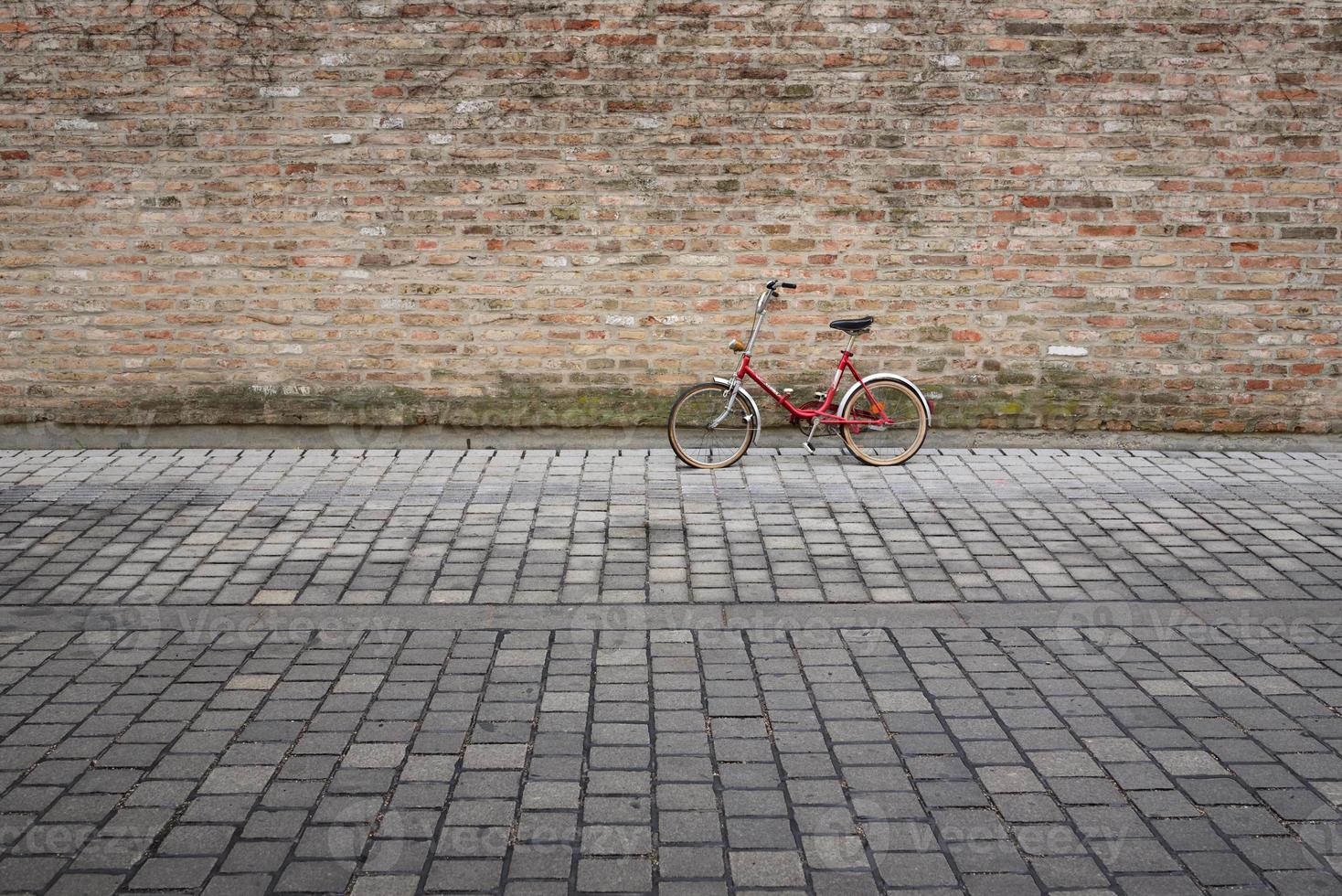 An old red bicycle leans against a brick wall in front of cobblestones, with space for text photo