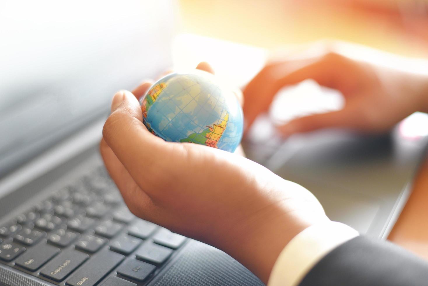Business man holding earth globe model in hand and use a laptop - Business technology global and around the world concept photo