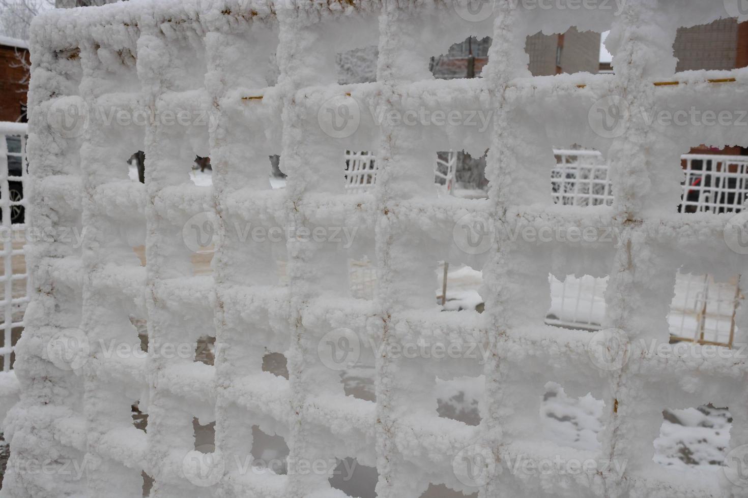 The fence grid is strewn with frost crystals, snowflakes. Winter snowy frosty background. World Snow Day photo
