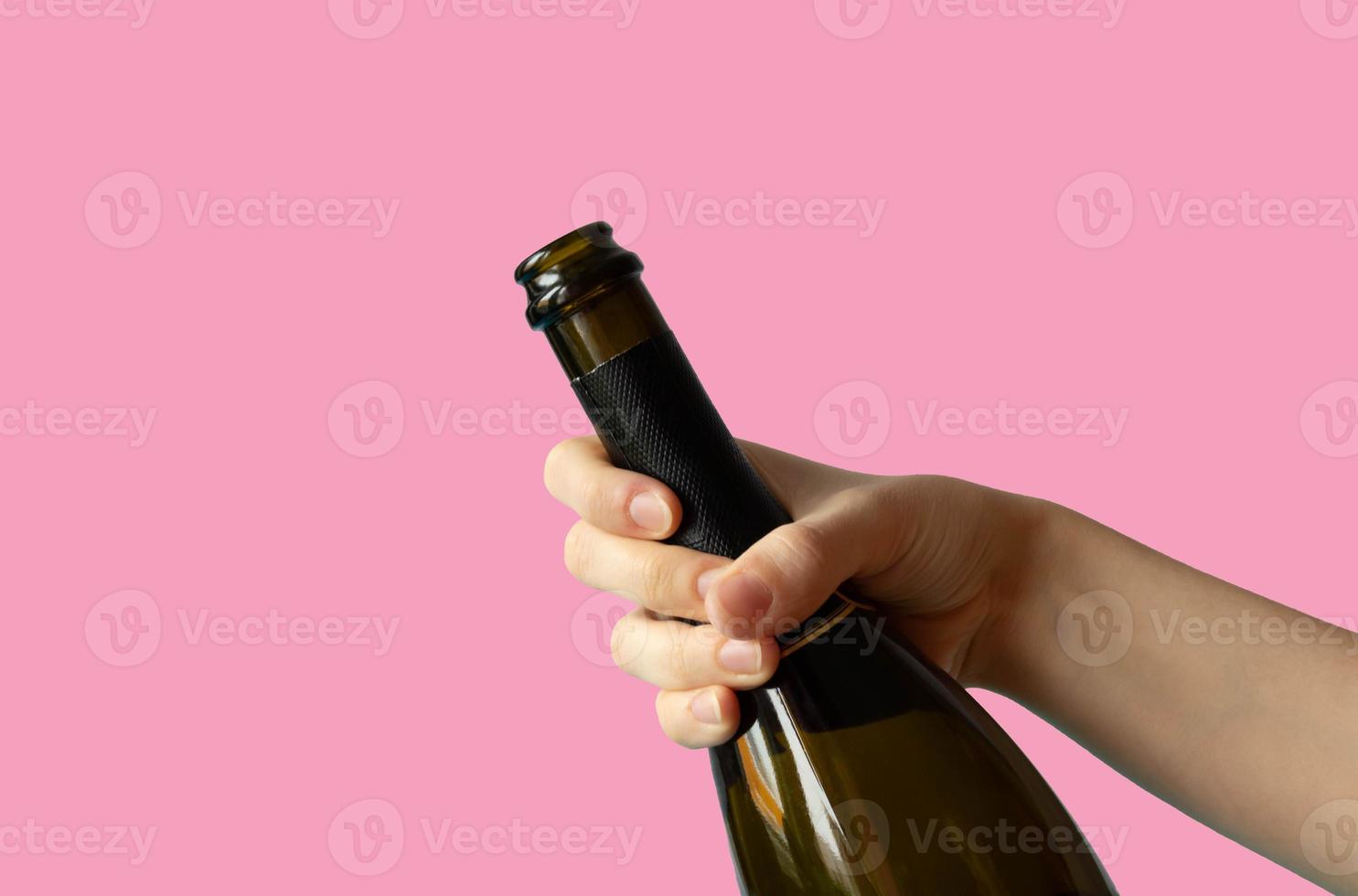 A woman's hand holding an open bottle of champagne on a pink background photo