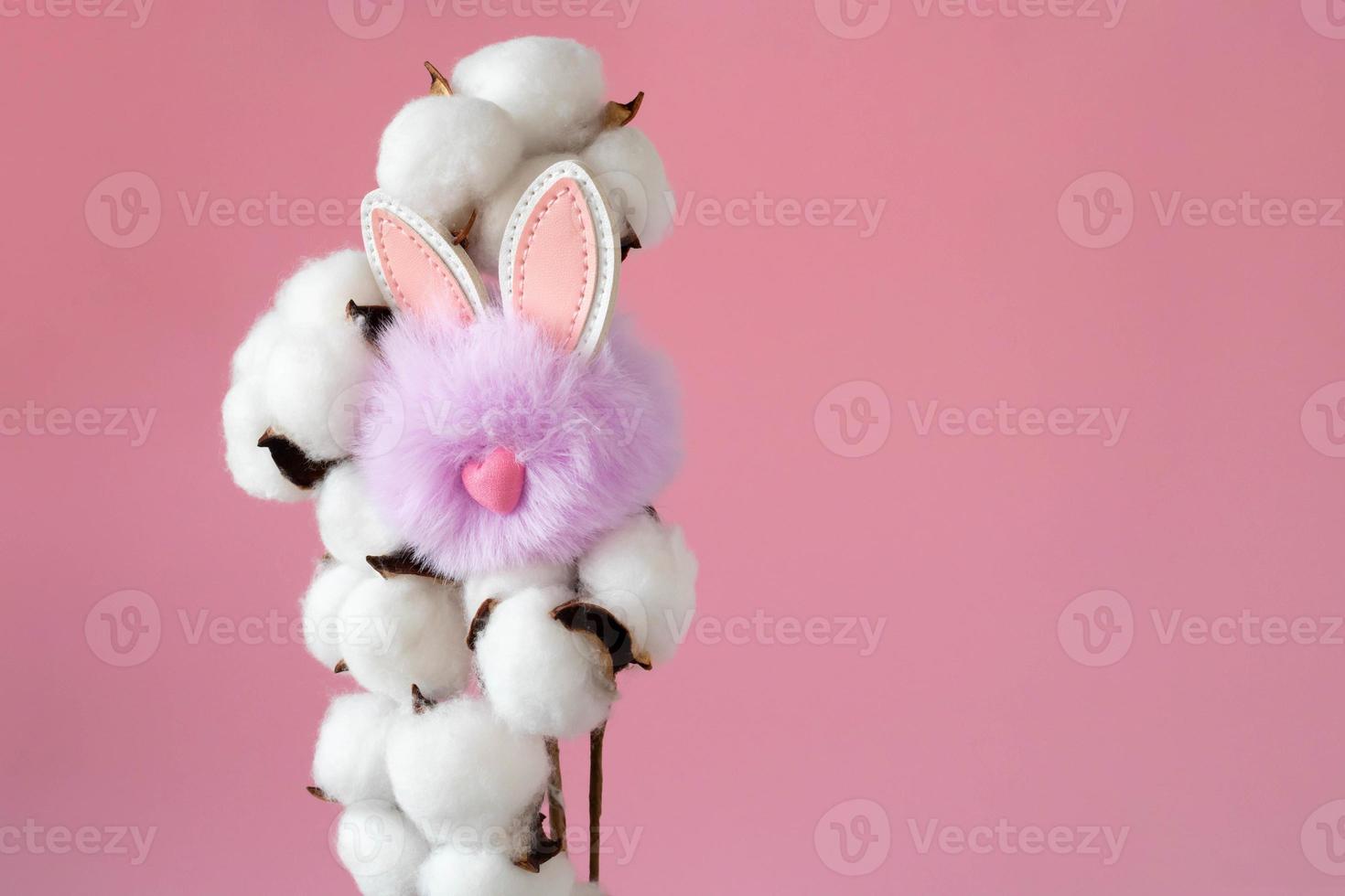 Beautiful white cotton flowers and a small fluffy lilac toy rabbit on a pink background. Easter Concept photo