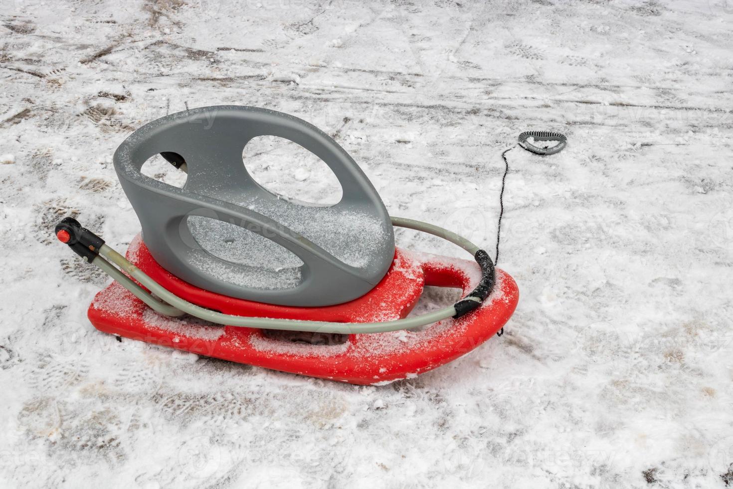 Red-gray plastic snow sled on the snow on the road photo